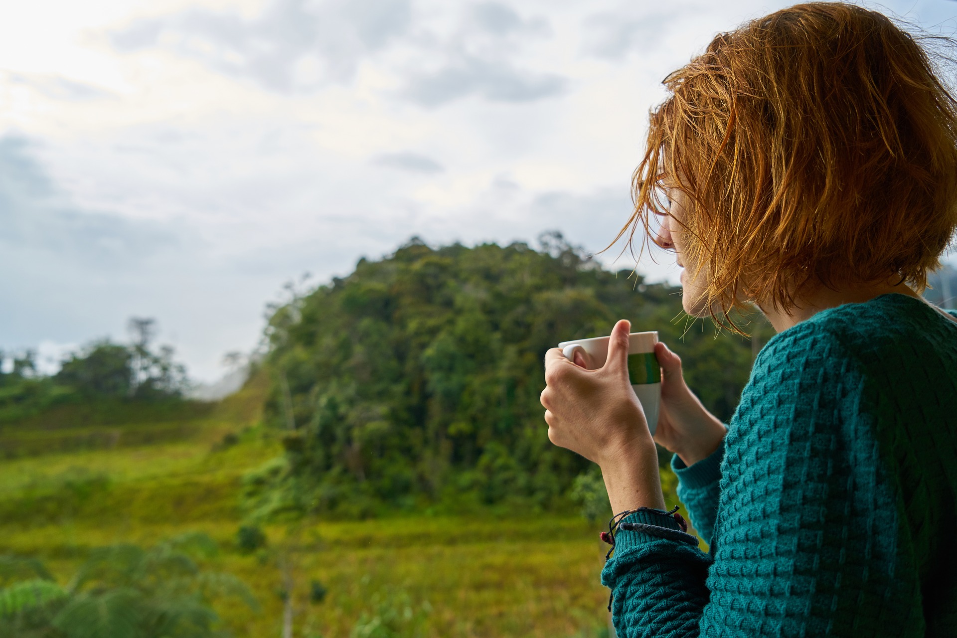 Kvinna som håller en kopp och tittar ut över landskapet.