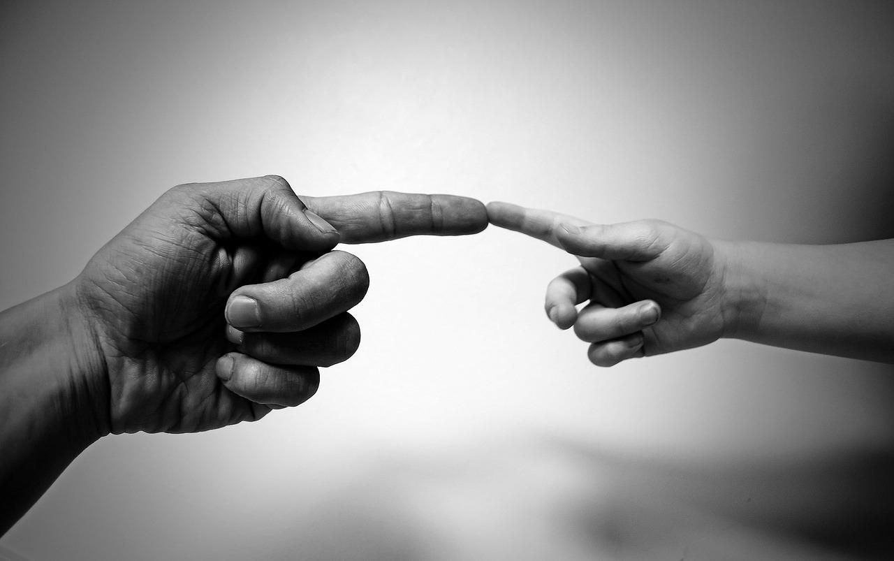 Två pekfingrar som möts från en vuxen person och ett barn.
